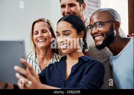 Questo momento deve essere catturato. Un gruppo di colleghi aziendali che scattano selfie con un tablet in ufficio. Foto Stock