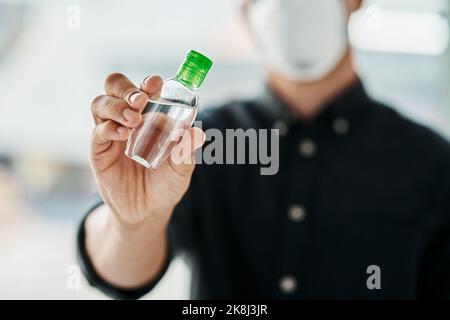 Un giovane uomo d'affari che indossa una maschera e usa l'igienizzatore per le mani. Foto Stock