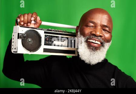 La musica è ciò che ci fa sentire giovani. Studio di un uomo anziano che tiene in mano una radio d'epoca su uno sfondo verde. Foto Stock