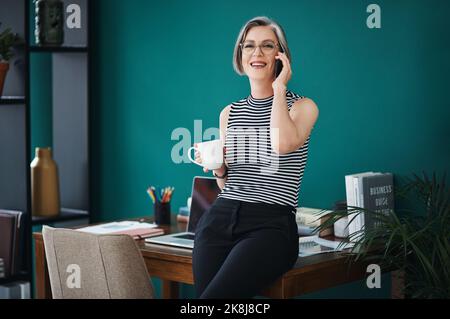Fate tutte le chiamate quando youre capo. Una donna d'affari che ha caffè mentre parla sul suo cellulare nel suo ufficio. Foto Stock