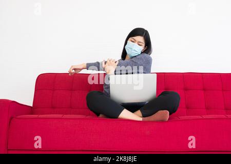 Donna stanca che indossa una maschera facciale, dolore ai muscoli del collo tendere e stretching, la sofferenza della sindrome da ufficio dopo lunghe ore di lavoro sul computer. Spento Foto Stock