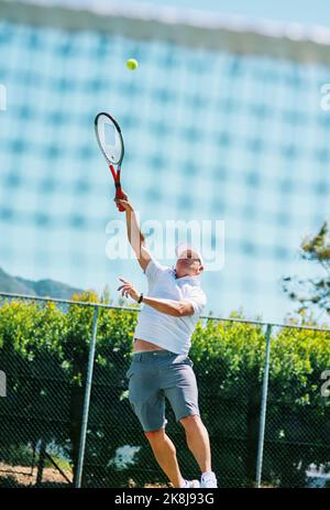 Ho una passione per il tennis. Un bell'uomo maturo che gioca a tennis da solo su un campo durante il giorno. Foto Stock