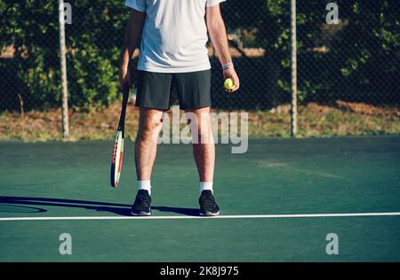 Mantenere la calma e servire un asso. Primo piano di un uomo irriconoscibile che tiene una racchetta da tennis e una palla su un campo da tennis. Foto Stock