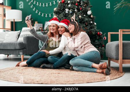 Una fantastica cartolina di Natale. Tre donne attraenti che prendono i selfie di Natale insieme a casa. Foto Stock