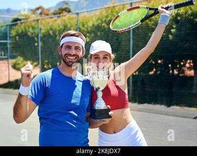 Un altro trofeo per la nostra mantelpiece. Ritratto corto di due giovani sportivi che si sono riuniti e che tengono un trofeo dopo aver vinto una partita di tennis. Foto Stock