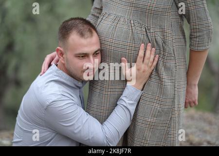 Padre sente il suo bambino nel ventre della donna in natura Foto Stock