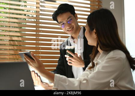 Giovane donna che condivide idee e strategie aziendali, spiegando nuove strategie sul tablet digitale alla sua collega Foto Stock