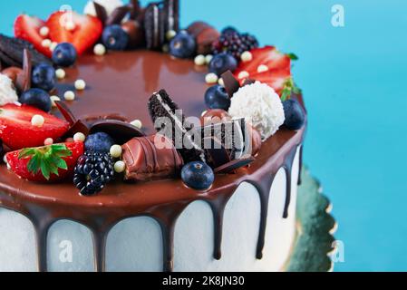 Torta di compleanno su sfondo blu. Primo piano di torta decorata con frutti di bosco freschi e dolci al cioccolato su sfondo colorato. Delizioso dessert per la festa Foto Stock
