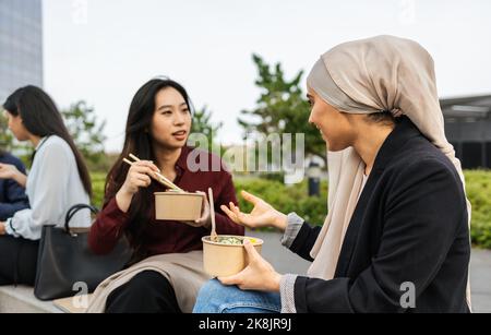 Le donne multirazziali di affari che prendono una pausa per mangiare un pasto fuori dell'ufficio Foto Stock