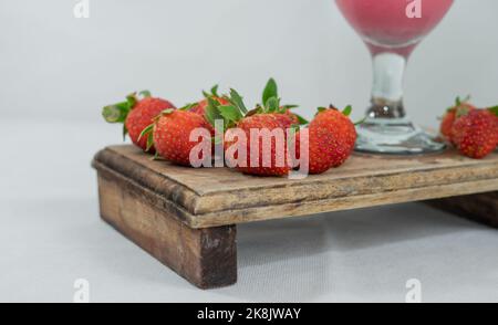 La vista parziale del bicchiere e delle fragole su un basamento di legno sulla superficie bianca Foto Stock