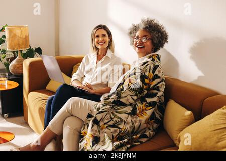 Allegre donne d'affari sorridenti felici mentre si siedono su un divano in un ufficio moderno. Due donne d'affari di successo che lavorano nella lobby di una donna di proprietà Foto Stock