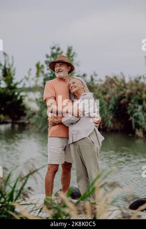 Felice coppia anziana che si abbraccia a piedi vicino al lago durante il giorno d'autunno. Foto Stock