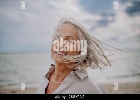 Ritratto di felice donna anziana con vento nei capelli, vicino al mare. Foto Stock