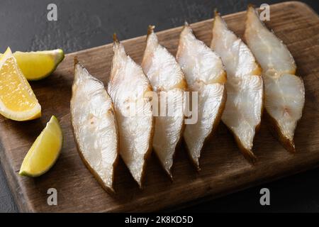 Deliziose fette di halibut affumicate servite con lime su sfondo nero. Primo piano. Spazio di copia. Foto Stock