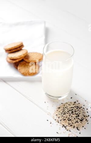 Cibo alternativo vegano, latte al sesamo non caseario su sfondo di legno bianco. Lattosa libera. Verticale. Foto Stock