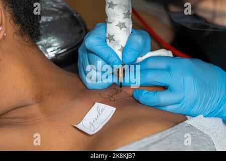 Artista tatuaggio che tiene in mano una macchina tatuaggio con guanti blu sterili e lavora in uno studio professionale Foto Stock