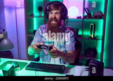 Giovane uomo redhead streamer giocare a videogame utilizzando il joystick nella sala giochi Foto Stock