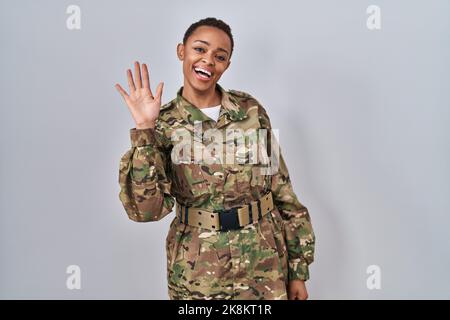 Bella donna afroamericana indossando mimetizzazione esercito uniforme rinuncia dicendo ciao felice e sorridente, amichevole gesto di benvenuto Foto Stock