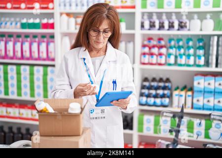 Farmacista donna di mezza età usando il touchpad che tiene il flacone di pillole in farmacia Foto Stock