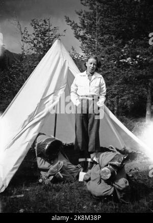 Norvegia, estate 1943 vita quotidiana durante la guerra. I permessi di viaggio erano difficili da raggiungere durante la seconda guerra mondiale, motivo per cui molti hanno scelto una bicicletta. Una giovane coppia ha affrontato il tratto Oslo / Ålesund. Donna con pantaloni lunghi e giacca bianca davanti alle tende bianche da pranzo. In primo piano zaini che contengono tutto ciò di cui hanno bisogno durante il viaggio. Foto: NTB Foto Stock