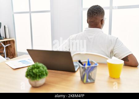 Giovane uomo africano che lavora in ufficio utilizzando un computer portatile in piedi indietro guardando lontano con le braccia sul corpo Foto Stock