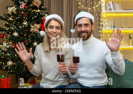 Coppia matura sposata uomo e donna che festeggia insieme Natale e Capodanno, guardando la webcam e sorridendo parlando con gli amici in videochiamata tenendo bicchieri da vino in mano che salutano a casa. Foto Stock