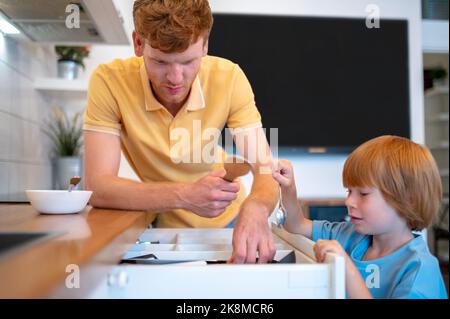 Zenzero giovane e suo figlio piccolo che fa colazione in cucina Foto Stock