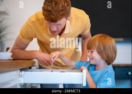 Zenzero giovane e suo figlio piccolo che fa colazione in cucina Foto Stock