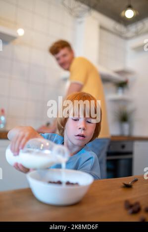 Zenzero giovane e suo figlio piccolo che fa colazione in cucina Foto Stock