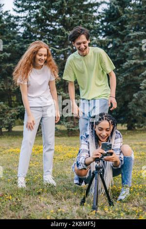 I giovani tre influencer che fissano il treppiede del telefono per fare un selfie sopra per i loro seguaci. Popolarità in internet, amicizia. Creazione di contenuti per Foto Stock