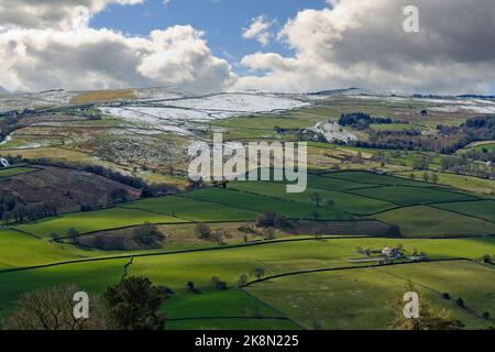 Vista dall'alto che guarda in una valle di campi verdi con un ripido pendio montuoso e neve in cima all'inizio della primavera, Nidderdale, Inghilterra, Regno Unito. Foto Stock