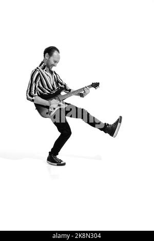 Ritratto di giovane uomo emotivo in abiti eleganti che suonano la chitarra, in posa isolata su sfondo bianco. Foto in bianco e nero Foto Stock