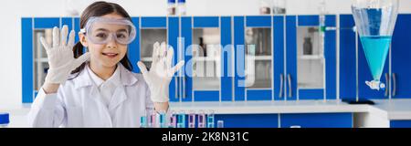 ragazza sorridente che mostra le mani in guanti in lattice in laboratorio chimico, banner, immagine stock Foto Stock