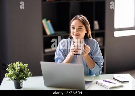 Bella giovane bruna donna che usa il computer portatile mentre lavora a casa bevande caffè. Foto Stock