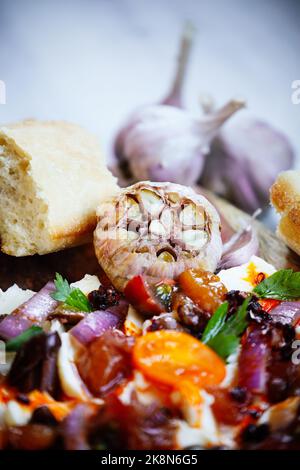 Bulbo d'aglio arrostito in olio e servito con un saporito pannello di burro e baguette. Messa a fuoco su bulbo con primo piano e sfondo sfocati. Foto Stock