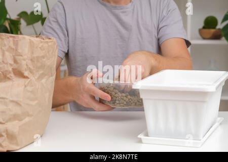 Un uomo si addormenta in una scatola di fiori di argilla espansa. Sporchi preparazione, il primo strato espanse creta. Preparazione per piantare piante. Giardinaggio a casa. Foto Stock