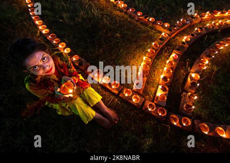 Narayanganj, Dhaka, Bangladesh. 24th Ott 2022. I devoti indù illuminano ''Diyas'' (lampade di terra) su un Rangoli, una cornice di motivi decorati, come parte dei festeggiamenti di Diwali in un tempio locale a Narayanganj, Bangladesh. Molte lampade o candele ad olio leggero per simboleggiare una vittoria della luce sulle tenebre, e fuochi d'artificio sono accesi come parte delle celebrazioni. Il festival si svolge ogni anno secondo il calendario lunare indù. Credit: ZUMA Press, Inc./Alamy Live News Foto Stock