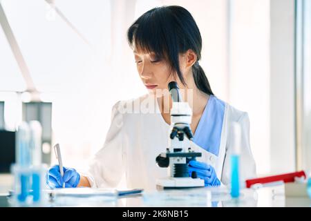 Ricercatore scienziato che lavora scrivendo le informazioni di analisi al moderno laboratorio di ricerca medica. Concetto di medicina, biotecnologia, microbiologia Foto Stock