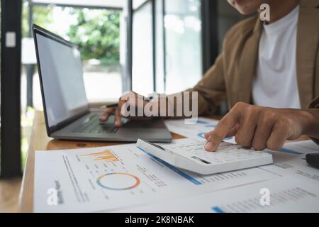 Uomo d'affari che utilizza il computer e la calcolatrice per calcolare i costi finanziari in ufficio. Foto Stock