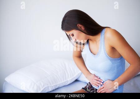 Dolore allo stomaco. Sotto sforzo. Donna piuttosto triste con un forte mal di testa nella sua casa seduta sul letto Foto Stock