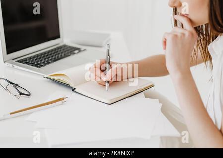 Donna irriconoscibile che prende appunti con una penna in un notebook aziendale. Foto Stock