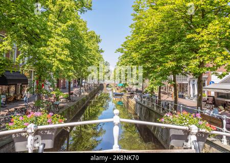 Residenti e turisti si godono lungo lo stretto canale nel centro della storica città di Delft. Foto Stock