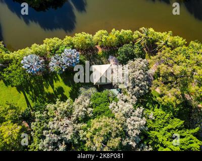 Ripresa aerea verso il basso della capanna tropicale accanto al fiume nel giardino botanico di Cairns Foto Stock