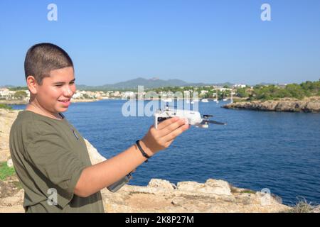 Primo piano, ragazzo felice, in preparazione per il volo con droni sulla costa mediterranea, contro il cielo blu durante il giorno di sole Spagna, Isole Baleari Foto Stock