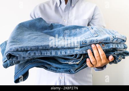 Pila di jeans nelle mani del venditore sullo sfondo chiaro Foto Stock