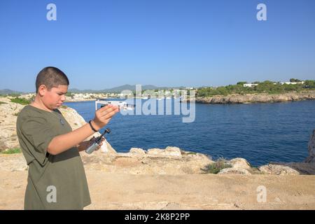 Ragazzo giovane felice, preparando e finalizzando i dettagli del volo per il volo con drone, concetto tecnologico Spagna, Isole Baleari Foto Stock