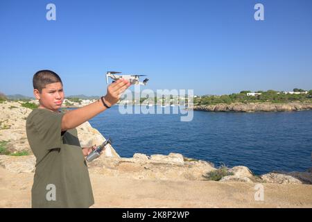 Ragazzo giovane felice, preparando e finalizzando i dettagli del volo per il volo con drone, concetto tecnologico Spagna, Isole Baleari Foto Stock