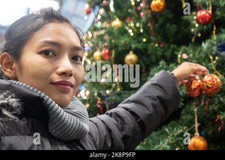 Una giovane donna in giacca invernale decorare un grande albero di Natale Foto Stock