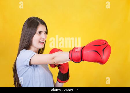 Giovane donna arrabbiata con guanti di boxe rossi si trova in posizione di combattimento, punzonando con la mano. Ritratto di ragazza forte e determinata preparato per la battaglia i Foto Stock