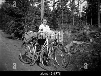 Norvegia, estate 1943 vita quotidiana durante la guerra. I permessi di viaggio erano difficili da raggiungere durante la seconda guerra mondiale, motivo per cui molti hanno scelto una bicicletta. Una giovane coppia ha affrontato il tratto Oslo / Ålesund. Donna in pantaloni lunghi e giacca bianca tiene entrambe le moto durante una sosta. Gli zaini sul vassoio portagagli contenevano tutto ciò che potevano immaginare durante il viaggio. Foto: NTB Foto Stock